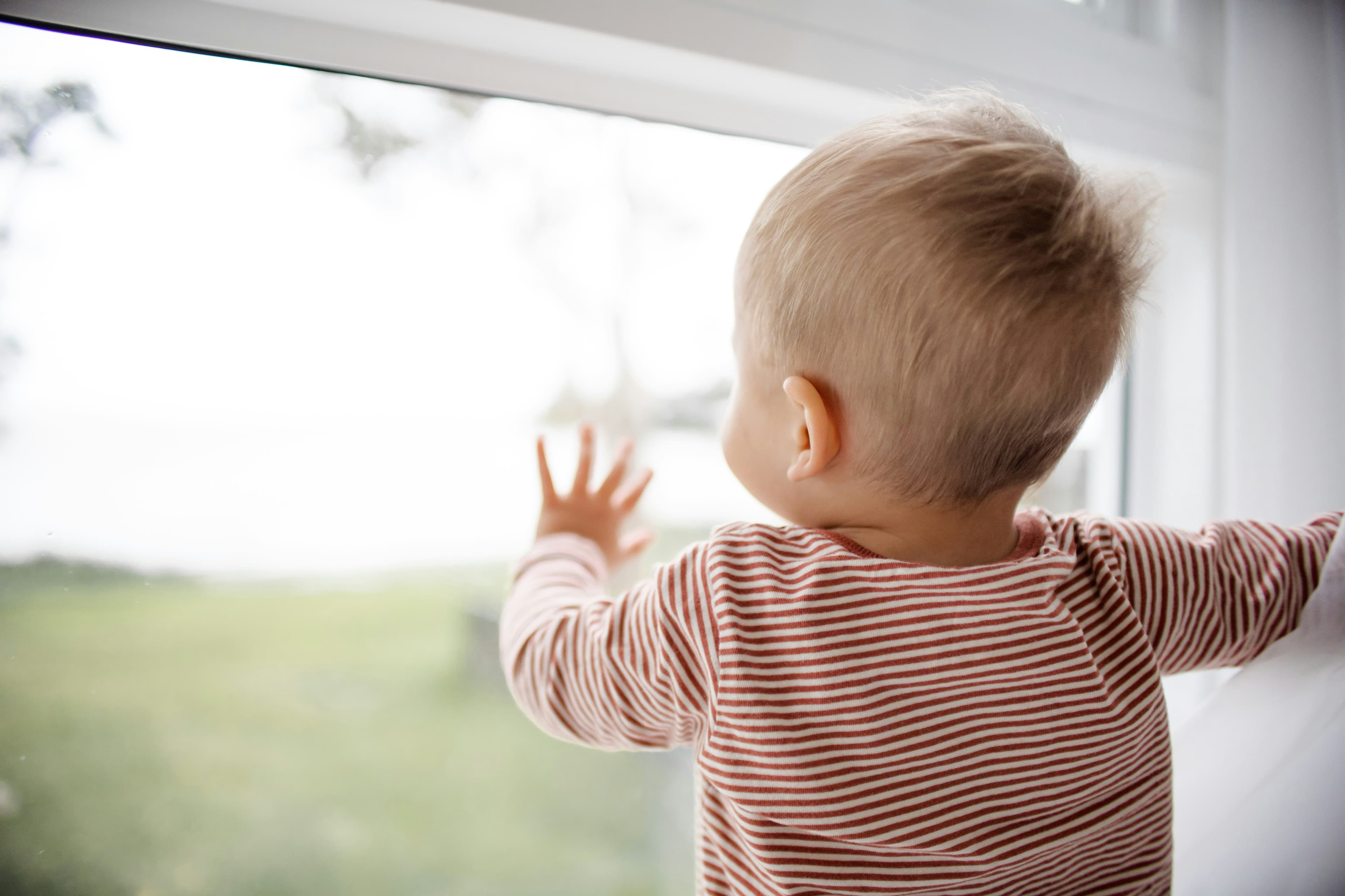 Toddler standing at a window, reaching up